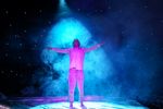 Ein Mann steht im pinken Licht mit ausgestreckten Armen auf der Bühne. Im Scheinwerferlicht sieht man den Nebel, der den Mann umgibt.