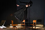 Eine schwarzgekleidete Frau balanciert auf einem Schulstuhl