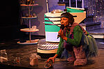 Elisabeth Frank als Jurrit in einem bunten Kostüm, vor einer Neonanzeige und einem Glitzervorhang singend 