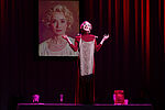 Eine blonde Frau in einem roten Hosenanzug singt auf einer Bühne