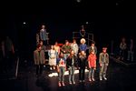 Eine Gruppe von Jugendlichen steht in zwei Reihen auf der Bühne neben- und hintereinander. Dahinter und daneben sind Podeste zu sehen, auf denen weitere Jugendliche stehen.
