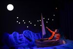 Eine Schauspielerin sitzt in einem kleinen Segelboot, hinter ihr die hellen Sterne, über ihr der Mond
