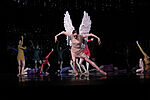 Eine Tänzerin mit Flügeln tanzt im Zentrum des Bildes um sie herum sind weitere Tänzer*innen