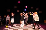 Eine Gruppe von Frauen steht auf einem schachbrettähnlichen Boden und spielt mit Luftballons, die in der Luft schweben.