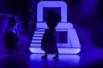 Zwei Figuren gehen im lila Licht vor einer Bühnenkonstruktion entlang.