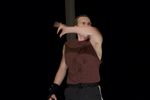 Ein Mann wirft seinen Arm vor sein Gesicht. Er trägt ein dunkles Oberteil, das mit dunklen Flecken versehen ist.