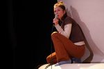 Eine Frau sitzt auf einer Erhöhung und hält ein Mikrofon an ihren Mund.