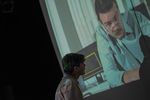 Ein Mann steht vor einer Videoprojektion, auf der ein Mann mit Brille zu sehen ist.