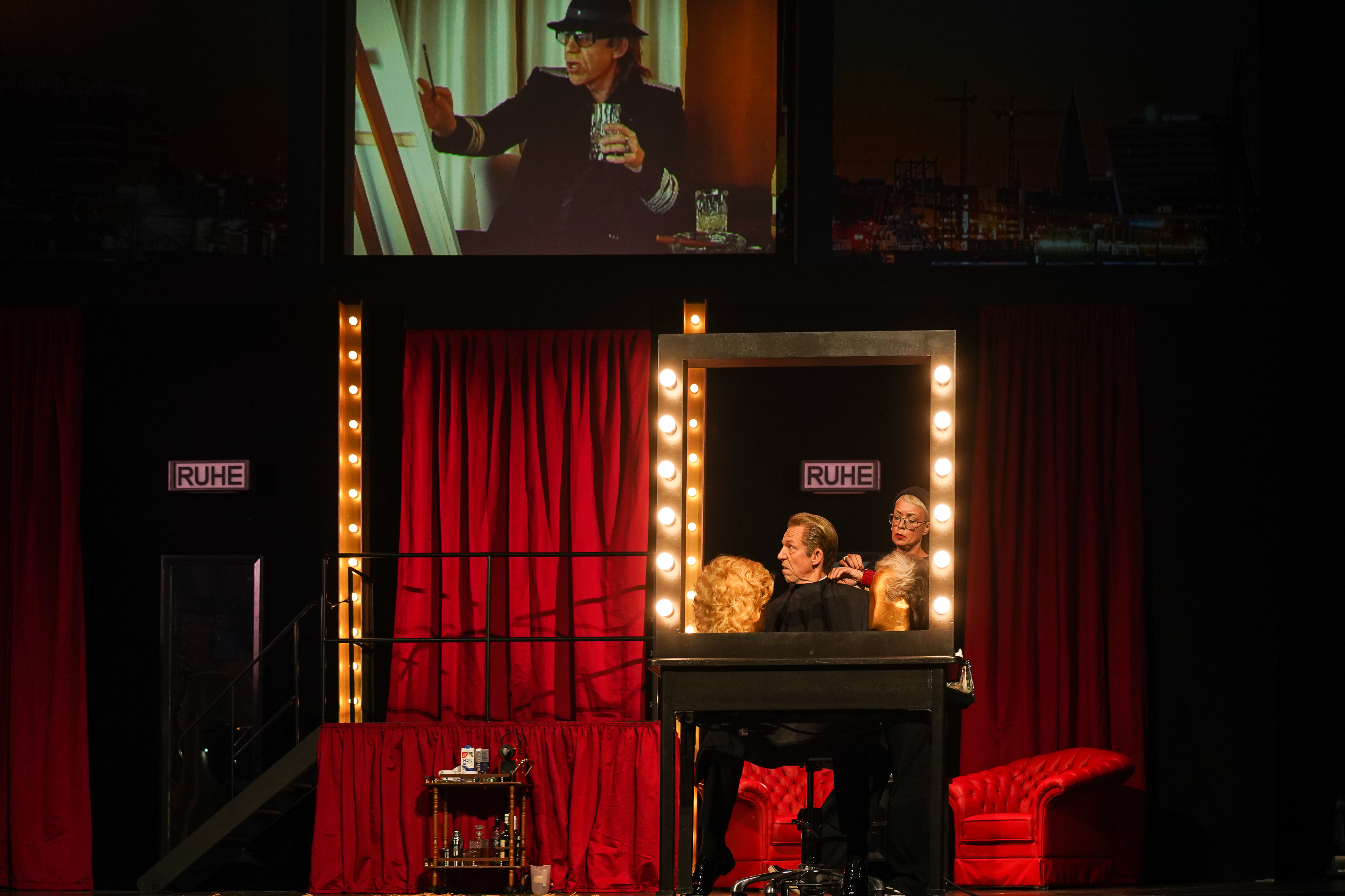 Showman sitzt unter einer Projektion von einer Udo Lindenberg Parodie